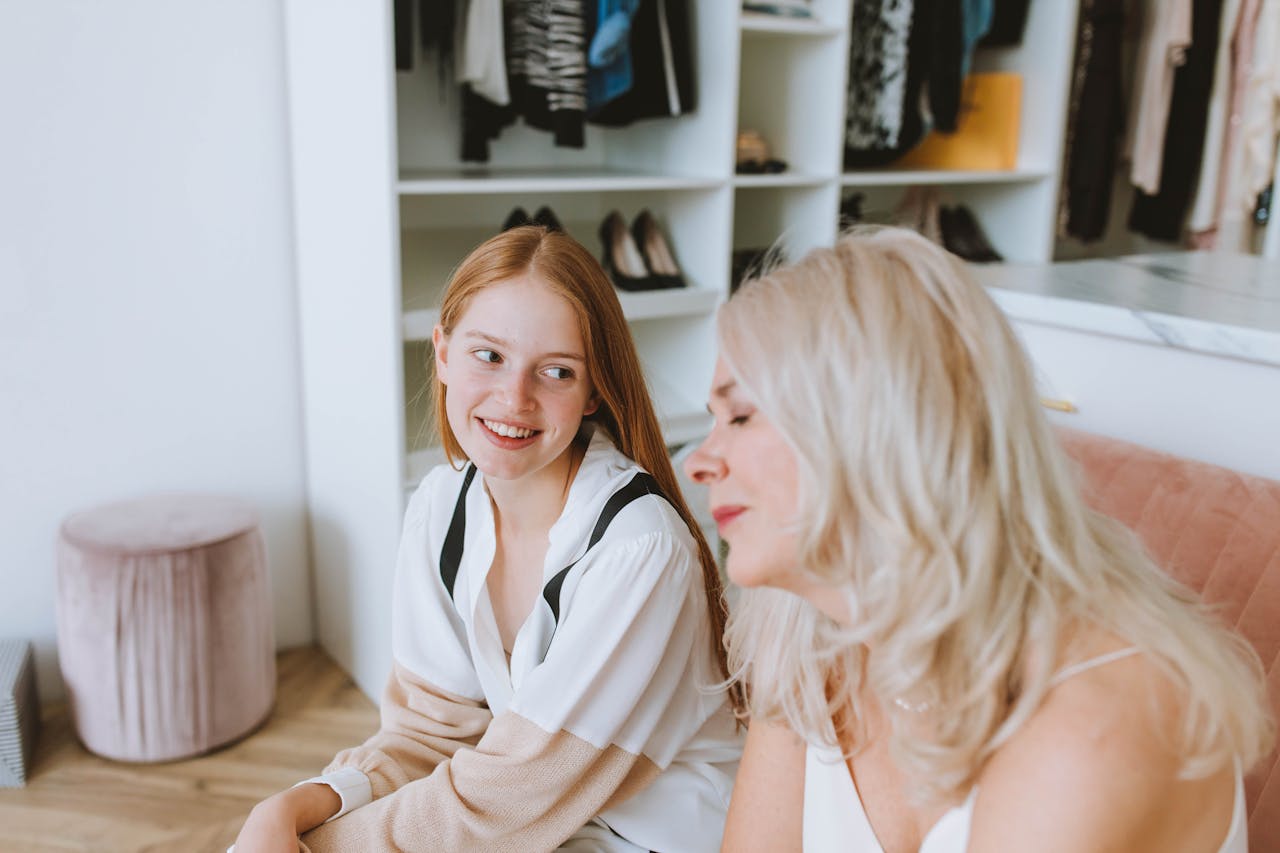 Two women smiling and bonding, seated in a modern wardrobe room, conveying positive emotions.