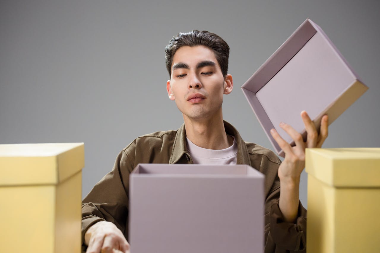 gallery-1 Asian man opening a gift box with a curious expression in a studio environment.